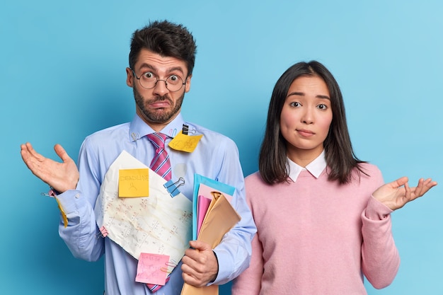 Hesitant coworkers shrug shoulders collaborate for making common task. Unaware clueless students dont know how to prepare project work successfully 