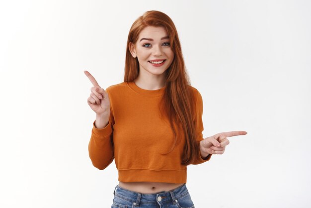 Hesitant cute lovely redhead stylish urban girlfriend asking opinion buy two products online shop pointing sideways left right look camera smiling awaiting suggestion what pick making choice