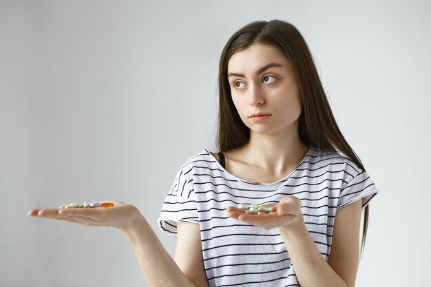 hesitant young dark haired woman can't decide between meds and vitamins