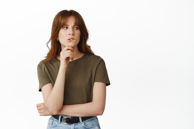 Hesitant young woman biting lip looking aside thoughtful have doubts while pondering or making choice standing indecisive against white background