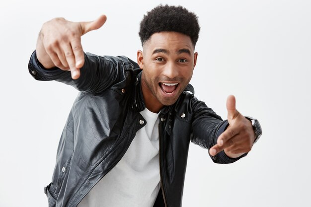 Hey, man. Positive emotions. Young good-looking black-skinned man with afro hairstyle in casual clothes pointing with hand in camera with excited face expression, posing for photo on party.