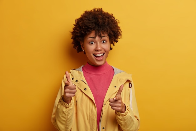 안녕,주의. 클라이언트 선택 개념. 행복 한 표정으로 긍정적 인 아프리카 계 미국인 여자 포인트, 뭔가를 선택, 누군가를 선택, 캐주얼 옷을 입고, 노란색 벽에 고립