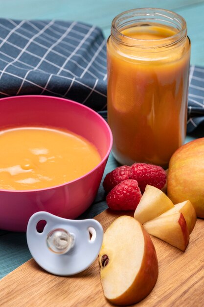 High angle of baby food in bowl with apples and pacifier