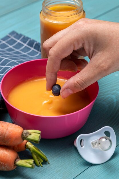 High angle of baby food in bowl with carrots and pacifier