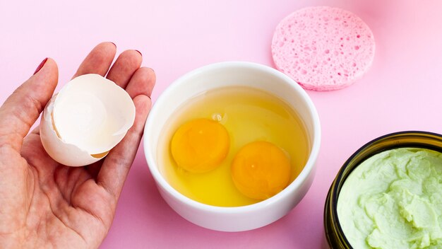 High angle of body butter and hand holding eggshell on pink background