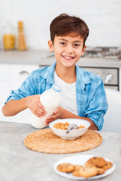 Высокий угол мальчик наливает молоко на зерновых