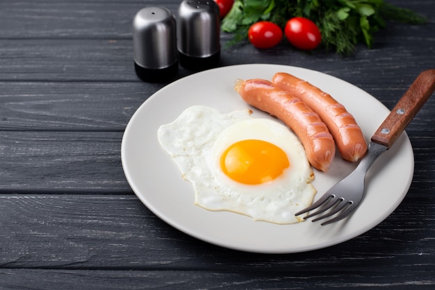 High angle of breakfast egg and sausages on plate with tomatoes and herbs