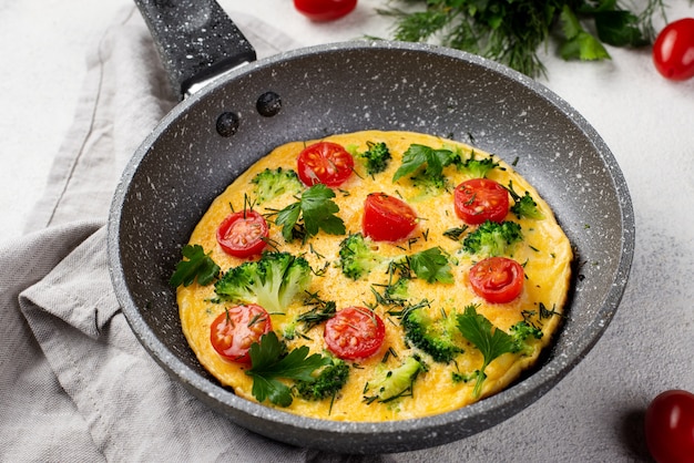 High angle of breakfast omelette in pan with tomatoes and herbs
