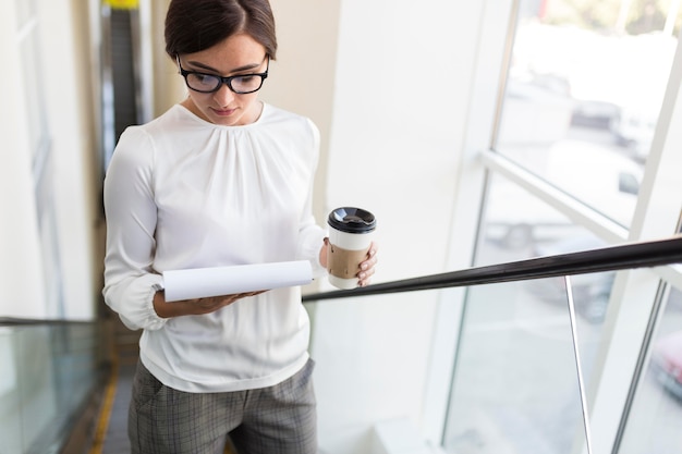 Free photo high angle of businesswoman on escalator with coffee and notepad