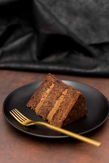 Высокий угол куска торта на тарелку с золотой вилкой