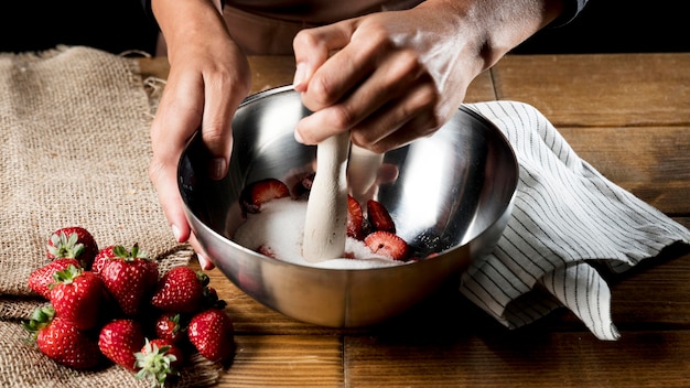 High angle of chef mixing strawberries and sugar in bowl