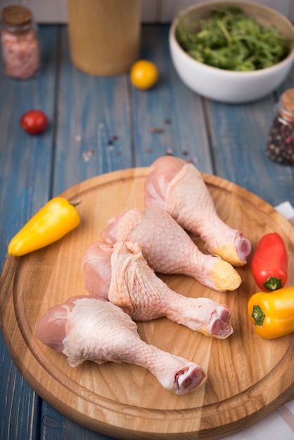 High angle chicken drumsticks on wooden board with peppers and tomatoes