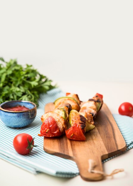 High angle chicken skewers on cutting board with tomato