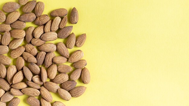 High angle closeup shot of almonds scattered on the left side of a yellow background