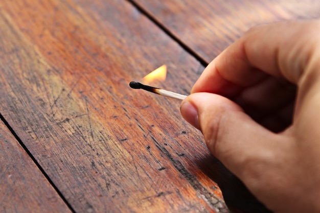 Free photo high angle closeup shot of a person holding a burning matchstick over a wooden surface