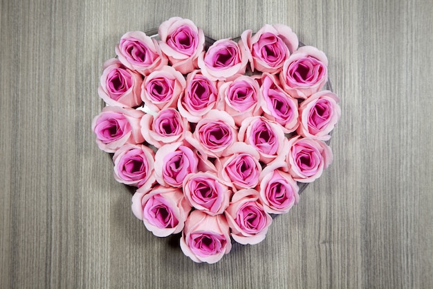 High angle closeup shot of pink roses in a heart shape on a wooden surface