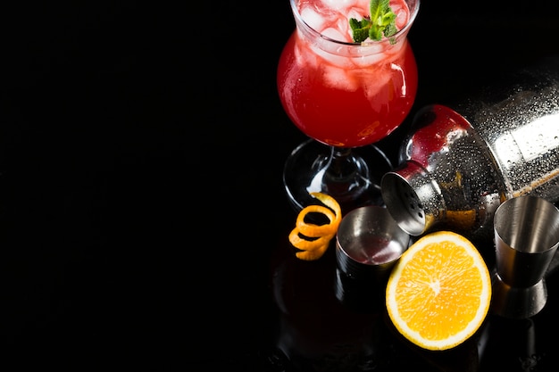 High angle of cocktail glass with shaker and orange