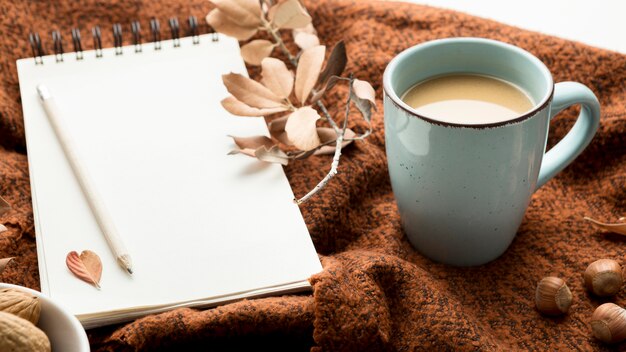 High angle of coffee mug with autumn leaves and notebook