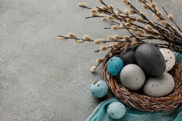 High angle of colored easter eggs in basket with copy space and twigs