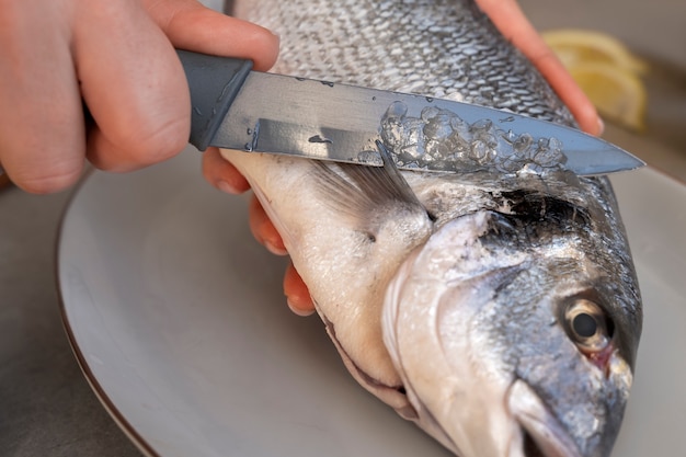 Foto gratuita cuoco ad alto angolo che pulisce il pesce in cucina