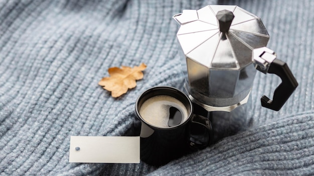 Free photo high angle of cup of coffee with kettle on sweater