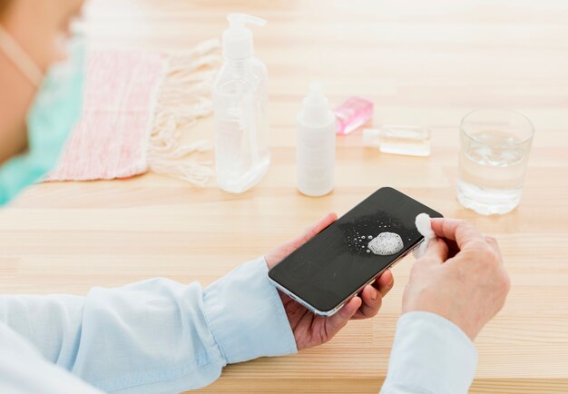 High angle of elder woman with medical mask disinfecting her smartphone