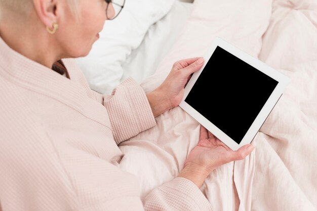 High angle of elderly woman in bed holding tablet