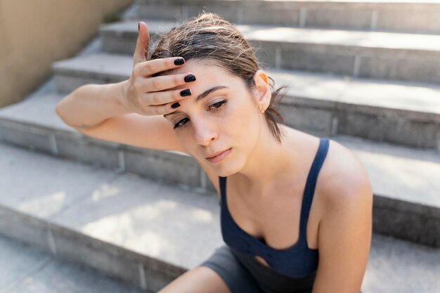 High angle of exhausted woman resting on stairs after exercising