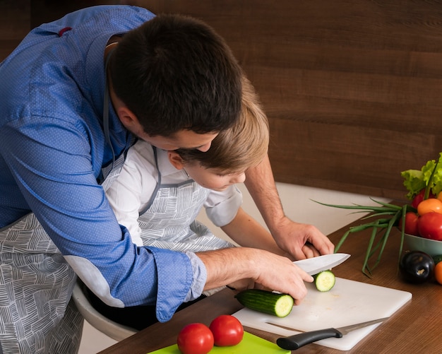 High angle father teaching son to cut vegetables