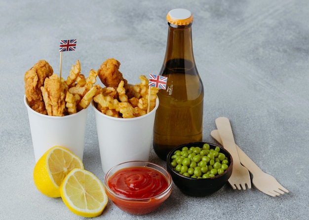 High angle of fish and chips in paper cups with great britain flags and beer bottle