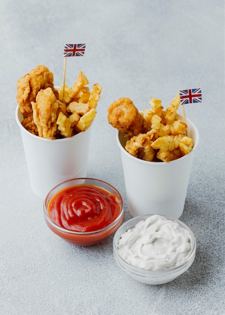 High angle of fish and chips in paper cups with great britain flags and sauces