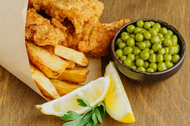 High angle of fish and chips in paper wrap with peas and sauce