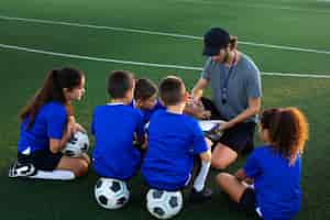 Бесплатное фото Тренер по футболу под большим углом обучает детей