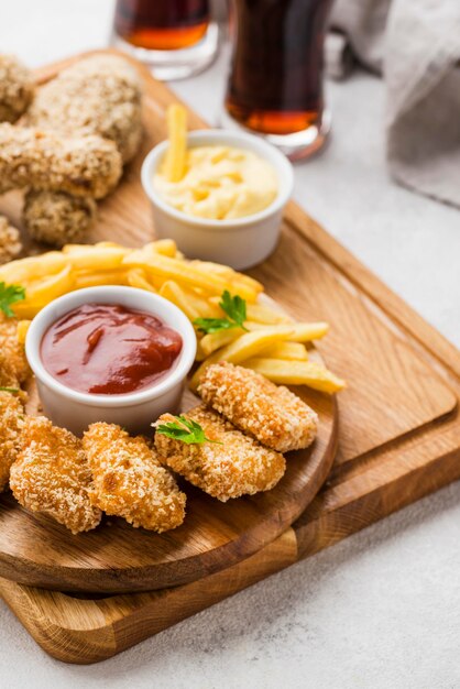 High angle of fried chicken legs and nuggets with fizzy drinks and french fries