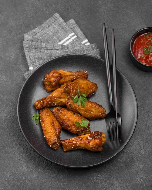 High angle of fried chicken parts on plate with cutlery and sauce