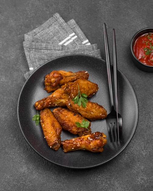 High angle of fried chicken parts on plate with cutlery and sauce