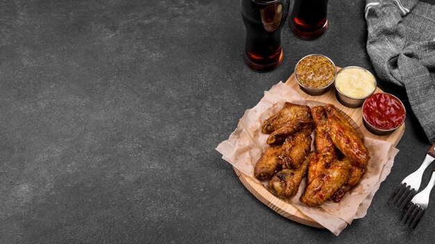 High angle of fried chicken wings with variety of sauces and fizzy drinks