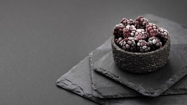 High angle of frozen blackberries in bowl with slate