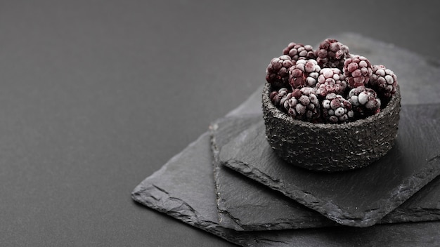 High angle of frozen blackberries in bowl with slate