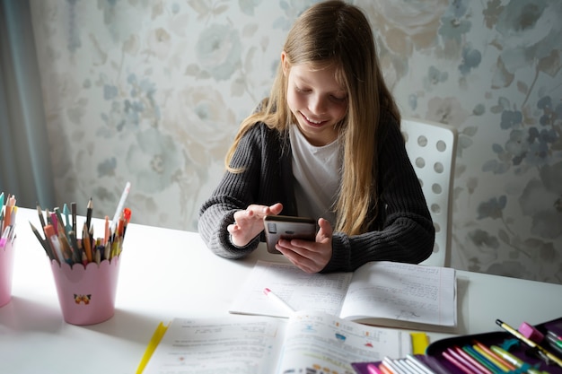 Девушка под высоким углом делает домашнее задание с телефоном