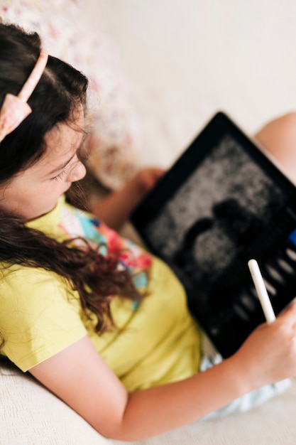 High angle girl sitting on the couch with tablet and pen