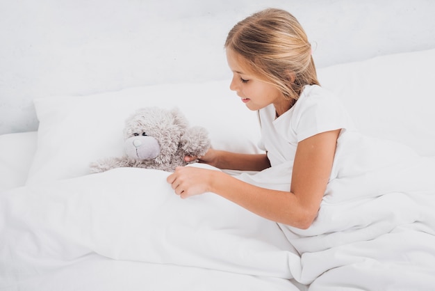 High angle girl staying in bed with her teddy bear