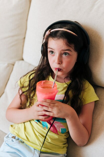 High angle girl with headphones drinking juice