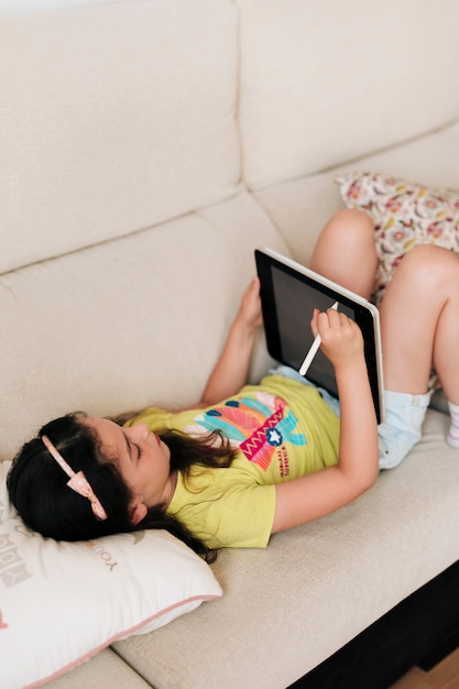 High angle girl with tablet sitting on the sofa