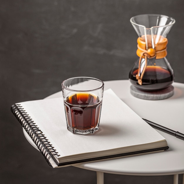 High angle of glass of coffee with notebook and pen