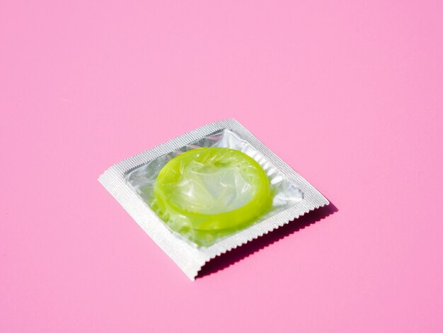 High angle green condom on pink background
