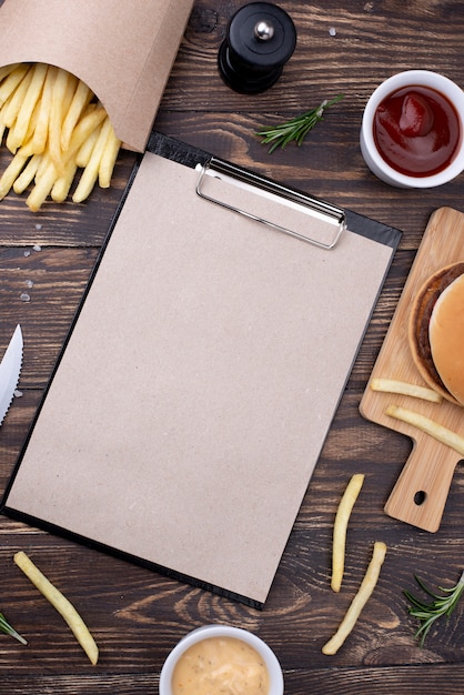 Hamburger di alto angolo con patatine fritte accanto a cliboard