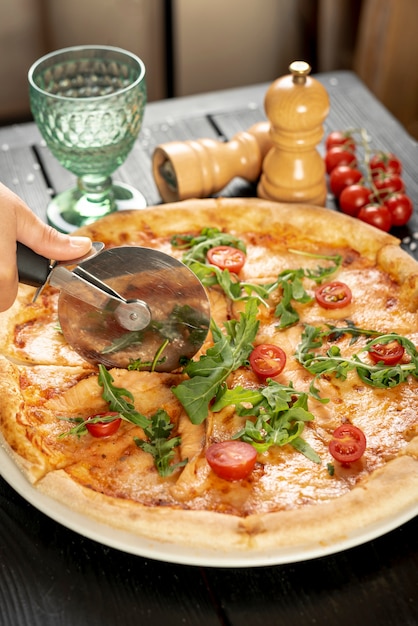 Free photo high angle of hand cutting pizza on wooden table