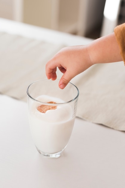 High angle hand dropping biscuit in milk