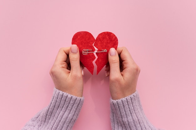 High angle of hand holding broken heart with safety pin